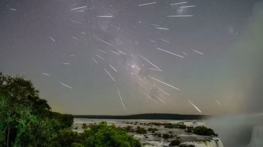 Visual noturno das Cataratas do Iguaçu, com a Via Láctea e uma chuva de meteoros visíveis no céu.