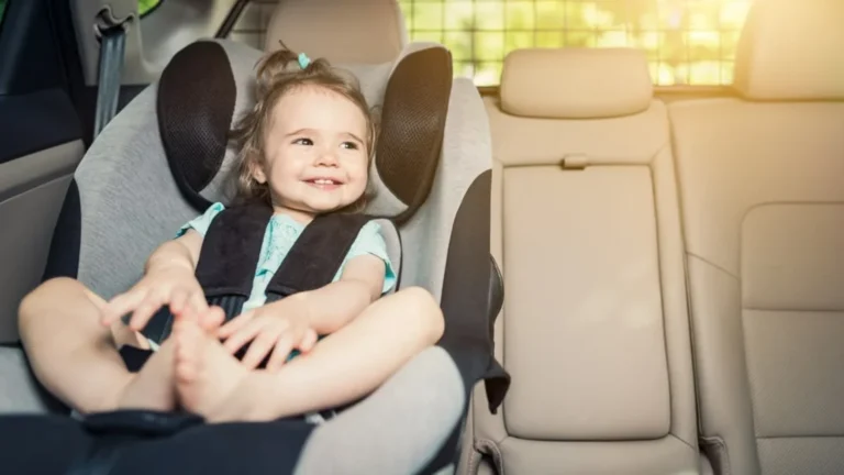 Uma criança pequena e sorridente sentada confortavelmente em uma cadeirinha de carro, pronta para viajar.