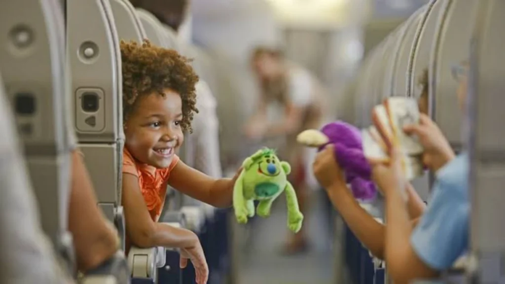 Duas crianças rindo e brincando com bonecos de pelúcia dentro de um avião, ilustrando a viagem de menores.