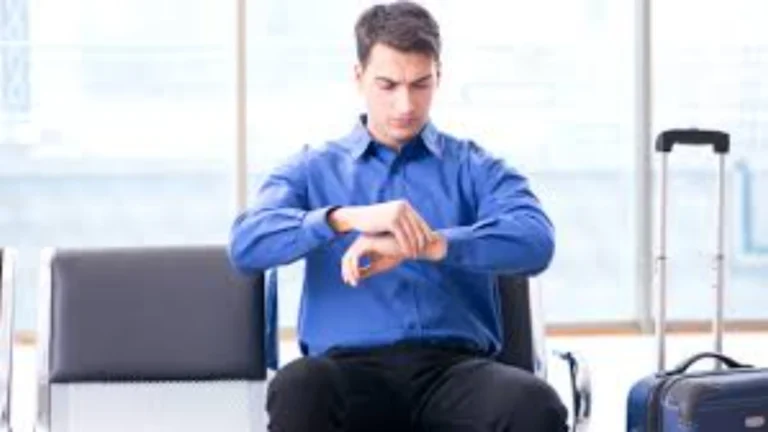 Um homem de camisa azul, visivelmente preocupado, olhando para o relógio enquanto está sentado em uma sala de espera ao lado