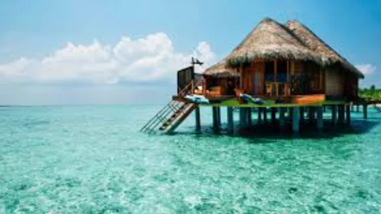 Bungalow de luxo sobre as águas cristalinas do oceano, com telhado de palha. Representa turismo regenerativo.